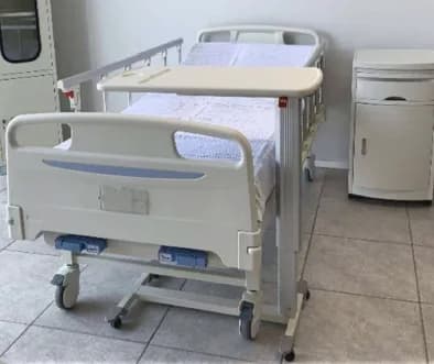 A manual hospital bed made up, with an over-bed table across it